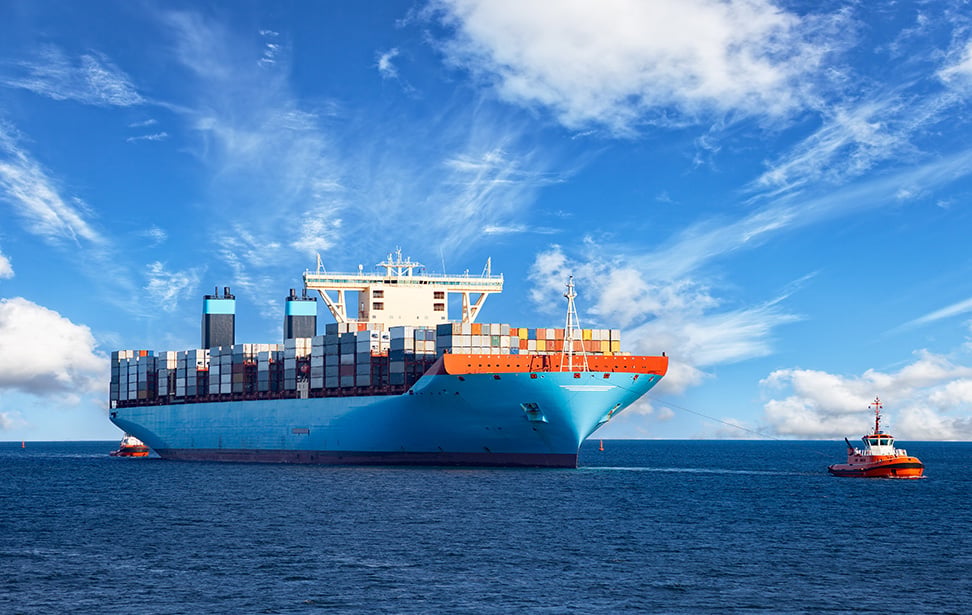 Photo of tugboat pulling large container ship at sea.
